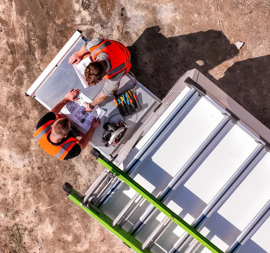 Aerial view of two MRT engineers reviewing build plans beside a canopy on the workshop floor